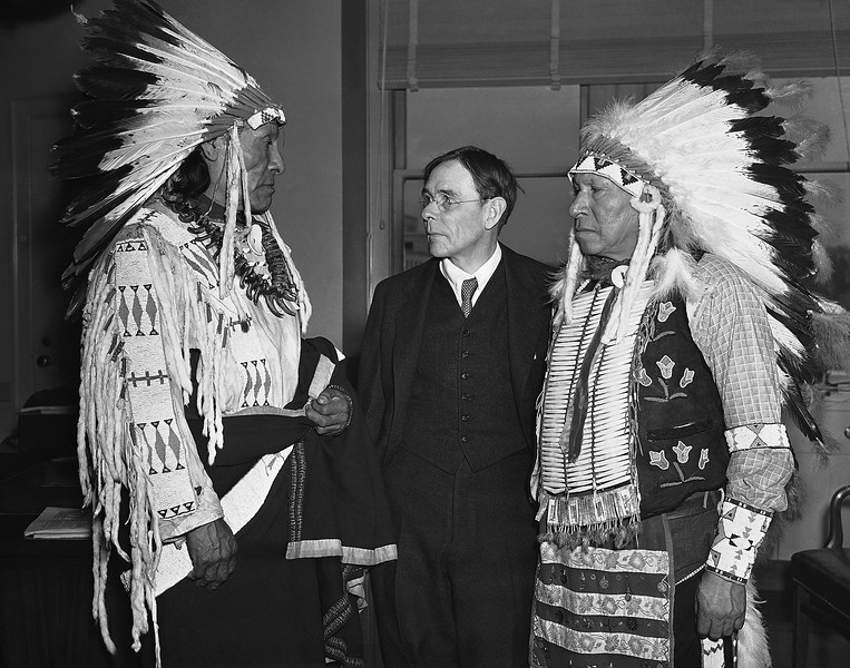 De izquierda a derecha Pájaro Dewie y Jaime-Pipa-en-la-Cabeza, supervivientes de la masacre de Wounded Knee, SD  son recibidos por un funcionario del Gobierno de los EEUU en Washington, DC el 4 de marzo de 1938,  compareciendo para solicitar indemnizaciones por la matanza.  Foto: Associated Press.